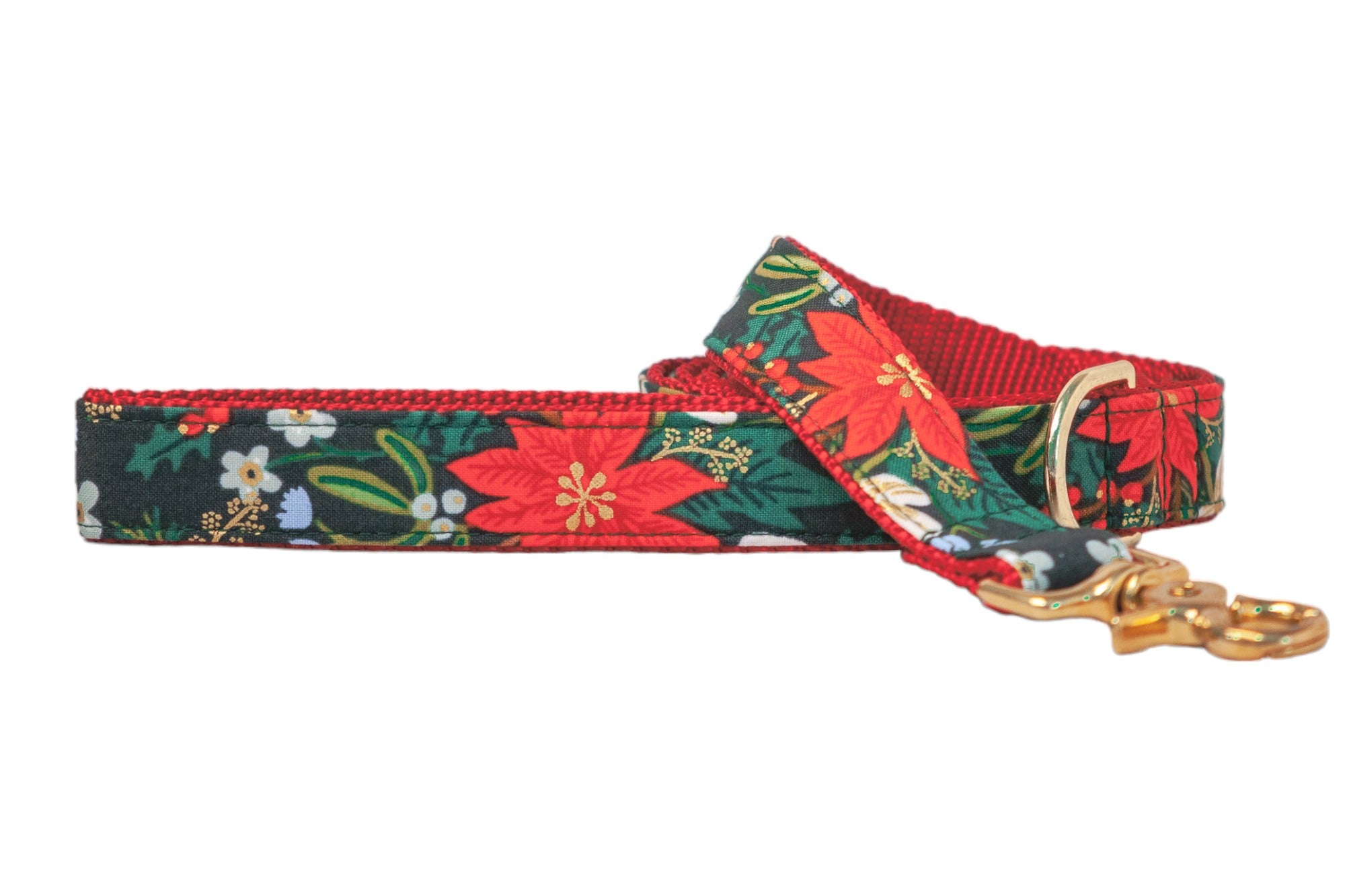Festive dog leash made from dark green fabric featuring a vibrant holiday floral print with poinsettias, light flowers, holly leaves, pinecones, and metallic accents. The leash is backed with nylon webbing and finished with shiny metal hardware including a D-ring and swivel clasp.