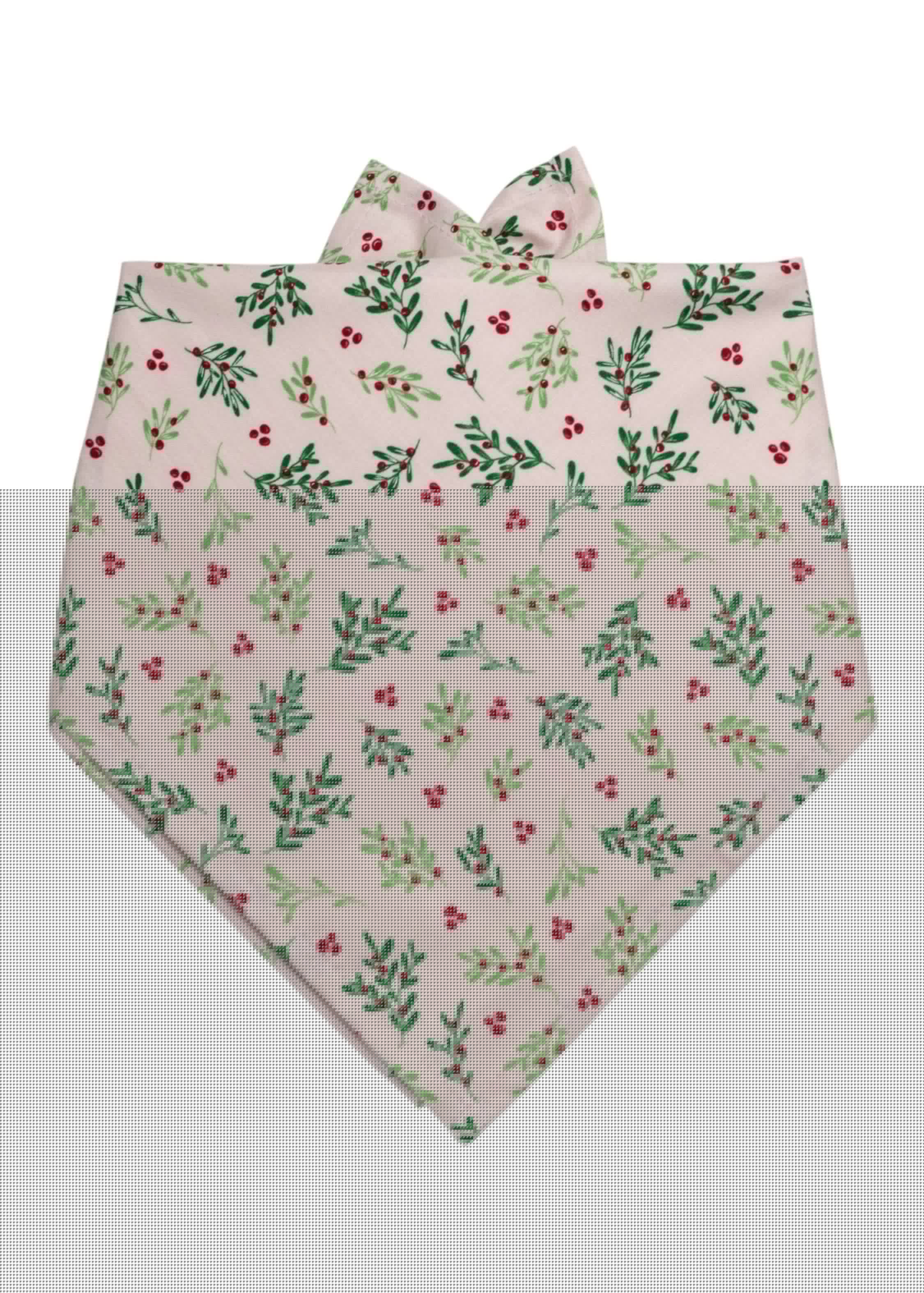 A festive dog bandana in a soft blush pink color, covered in a repeating botanical print of foliage and berries. The triangular fold allows it to be tied comfortably around a dog's neck, with visible folds at the top and a pointed bottom edge that adds a stylish finishing touch.